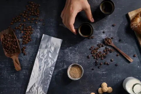 Kaffeebohnen, eine leere Vakuumverpackung für lange Haltbarkeit, Zucker und zwei Espressotassen.