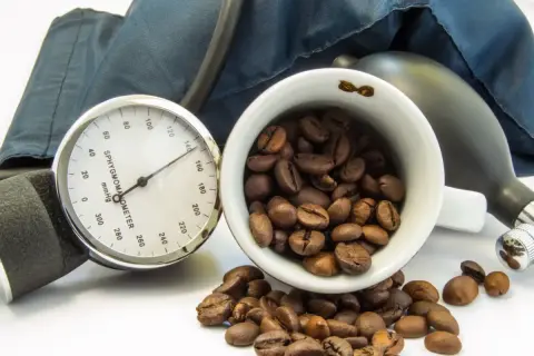 Blutdruckmessgerät und Kaffeebohnen. Die Frage, ob Kaffee senkt den Blutdruck, wird hier visuell thematisiert.
