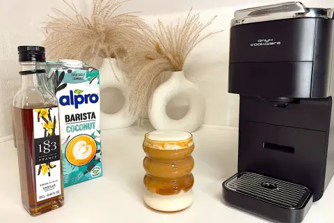 Ein leckerer Kokosnuss-Latte mit Alpro Barista Coconut, Vanillesirup und einer Kaffeemaschine.