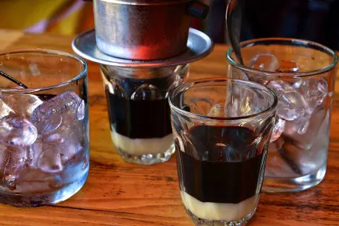 Zwei Gläser mit süßer Kondensmilch und starkem Kaffee, bereit für Eiswürfel. Ein vietnamesischer Eiskaffee zum Genießen.