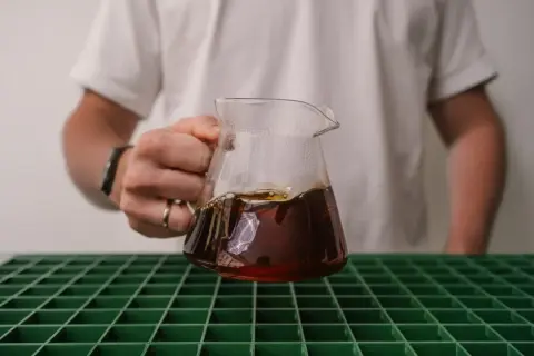 Person hält ein Glasgefäß mit frisch gebrühtem Kaffee, der gerade extrahiert wurde.
