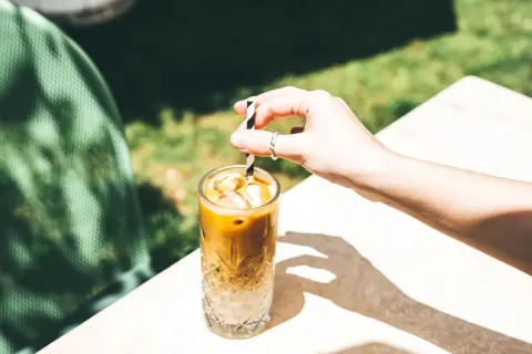 Erfrischender Eiskaffee ohne Eis, mit einem gestreiften Strohhalm, der in einem Glas mit Eiswürfeln steckt.