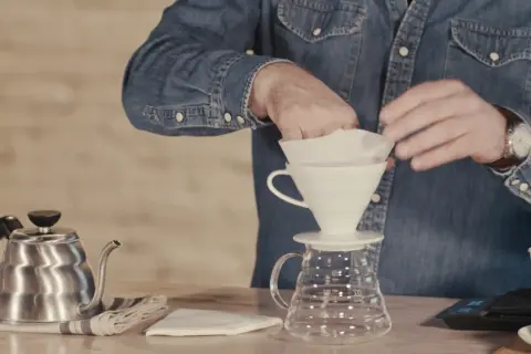 Mann bereitet sich auf das Kaffee filtern vor, indem er den Papierfilter in den Trichter legt.