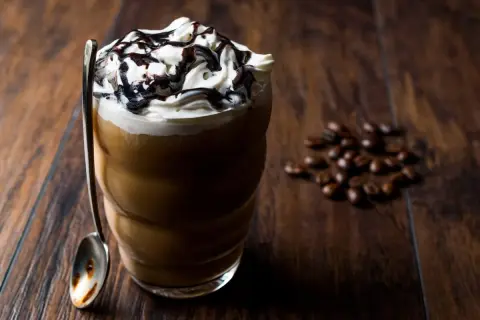 Eisgekühlter Kaffee mit Sahne und Schokoladensauce, ein köstliches Frappuccino Rezept. Daneben liegen geröstete Kaffeebohnen.