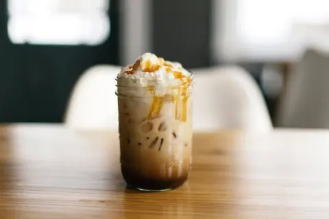 Ein köstlicher Caramel Frappuccino mit Sahne und Karamellsauce, serviert in einem Glas auf einem Holztisch.