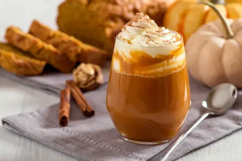 Ein cremiger Pumpkin Spice Latte mit Sahne und Zimt, daneben Kürbisbrot und Zimtstangen. Ein Genuss, der die pumpkin spice latte kalorien vergessen lässt.