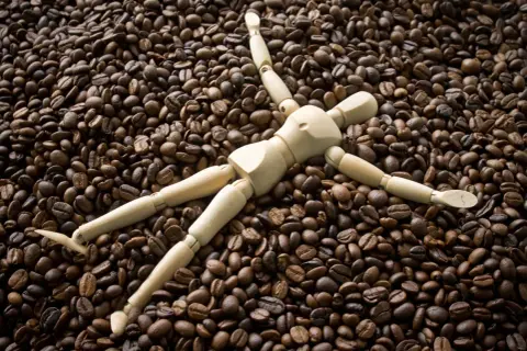 Holzfigur liegt auf einem Berg gerösteter Kaffeebohnen. Sieht aus, als würde sie die Kaffeebohnen kauen.