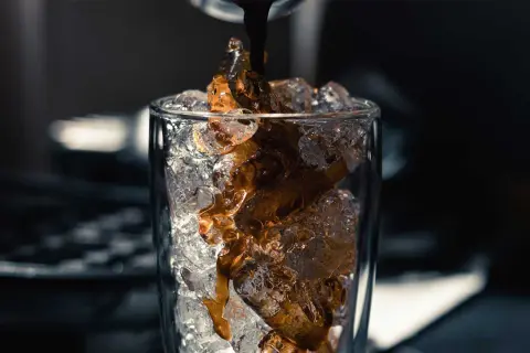 Heißer Espresso fließt auf Eiswürfel in einem Glas. Perfekt für ein erfrischendes iced americano rezept.