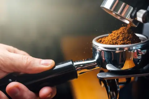 Frisch gemahlener Kaffee für den perfekten espresso geschmack. Eine Hand hält den Siebträger, während feines Kaffeepulver hineinfällt.