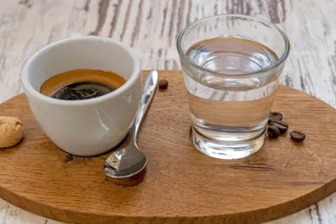 Ein Espresso mit einem Glas Wasser, einem Keks und Kaffeebohnen. Das Wasser ist wichtig, um den Gaumen zu reinigen und den vollen Geschmack des Espressos zu genießen.