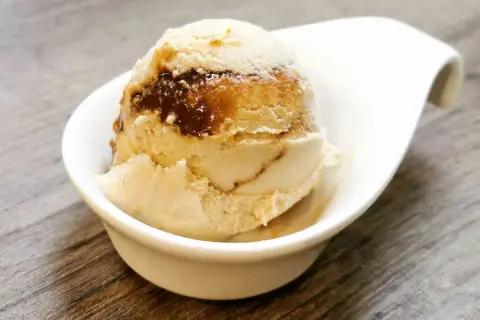 Cremiges Eis mit Karamellsauce, das an einen iced macchiato erinnert, in einer weißen Schale auf Holztisch.