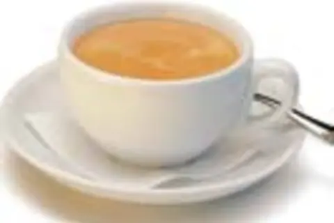 Eine Tasse mit cremigem, braunem Kaffee steht auf einer Untertasse. Ein kleiner Löffel liegt daneben.