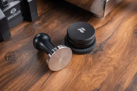 Ein Tamper ist ein Werkzeug zum Verdichten von Kaffeepulver im Siebträger. Hier liegt ein schicker Tamper neben einem Kaffee-Dosierring.