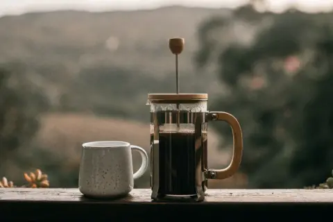 Eine French Press, bereit für den perfekten Kaffee. Neben einer Tasse wartet sie auf den Genuss.