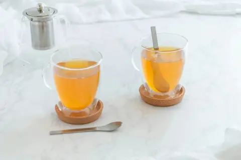 Zwei Tassen mit warmem Tee, ideal bei Halsschmerzen. Ein Teekännchen steht im Hintergrund.