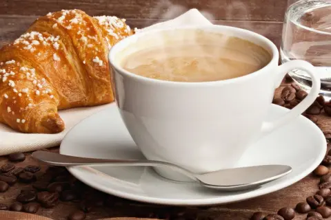 Dampfender Cappuccino mit Croissant und Kaffeebohnen. Ein Genuss, der die **Cappuccino Kalorien** wert ist.