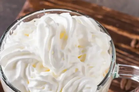 Ein Glas mit cremigem Cappuccino con panna, bedeckt mit einer üppigen Haube aus Schlagsahne.