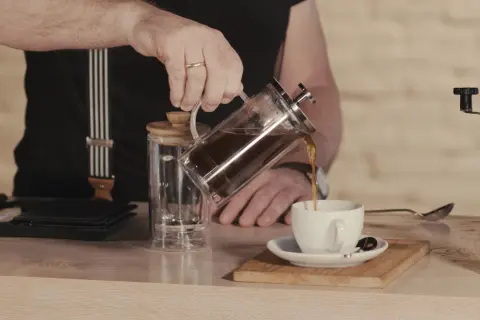 Mann gießt French Press Kaffee in eine Tasse. Die Menge ist für 2 Tassen ausgelegt.