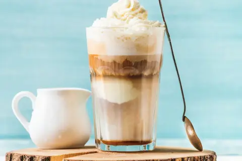 Ein cremiger Eiskaffee Karamell mit Sahnehaube, daneben ein Milchkännchen.