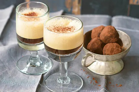 Zwei Gläser mit cremigem Caffe Shakerato, bestäubt mit Kakao. Daneben eine Schale mit Schokoladentrüffeln.