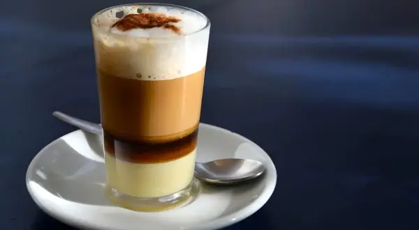 Ein geschichteter Kaffee mit Kondensmilch, Espresso und Milchschaum, bestreut mit Zimt. Ein süßer Genuss, wie ein flüssiger bonbon kaffee.