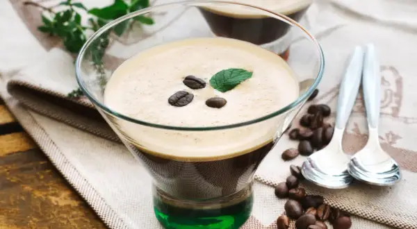 Ein köstlicher Eiskaffee italienisch, garniert mit Kaffeebohnen und Minze, serviert in einem Glas mit grüner Likörschicht.