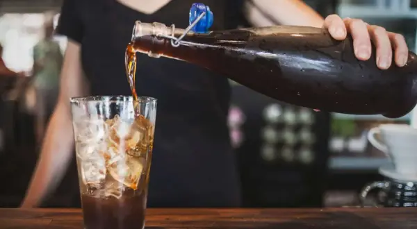 Eine Person gießt Cold Brew Kaffee mit Eis in ein Glas. Cold Brew ist ein Kaffee, der kalt extrahiert wird.