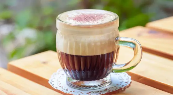 Ein Glas mit cremigem Kaffee mit Ei, bestäubt mit Kakao, steht auf einem Holztisch.