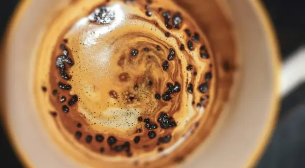 Nahaufnahme einer Tasse Kaffee mit Crema und Kaffeepulver, die an die Herstellung von Instantkaffee erinnert.
