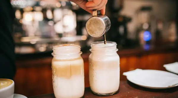 Zwei Latte Macchiato in Gläsern, ein Barista gießt Espresso ein. Kalorienbewusst genießen?