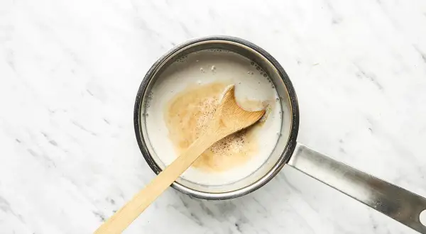 Ein Holzlöffel rührt in einem Topf mit cremiger Hafermilch, die für einen köstlichen Hafermilch-Latte vorbereitet wird.