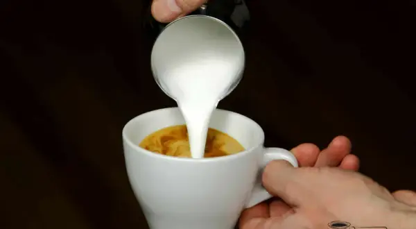 Milch wird in einen Espresso gegossen, um einen perfekten Espresso macchiato zu kreieren.