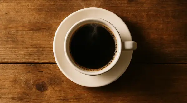 Eine Tasse dampfender schwarzer Kaffee auf einem Holztisch. Schwarzer Kaffee hat kaum Kalorien, perfekt für eine bewusste Ernährung.