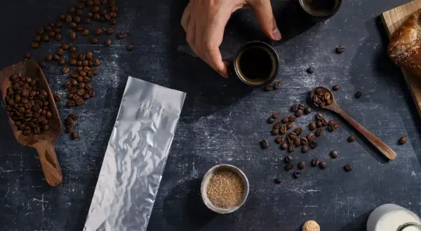 Kaffeebohnen, eine leere Vakuumverpackung für lange Haltbarkeit, Zucker und zwei Espressotassen.