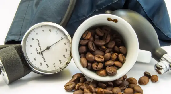 Blutdruckmessgerät und Kaffeebohnen. Die Frage, ob Kaffee senkt den Blutdruck, wird hier visuell thematisiert.
