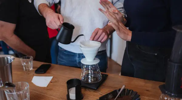 Hände bereiten Kaffee zu, die **Koffeinwirkung** wird bald spürbar sein. Wasser fließt in einen Filter über einer Karaffe.