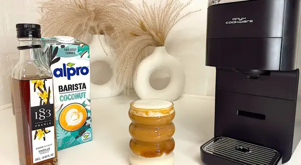 Ein leckerer Kokosnuss-Latte mit Alpro Barista Coconut, Vanillesirup und einer Kaffeemaschine.