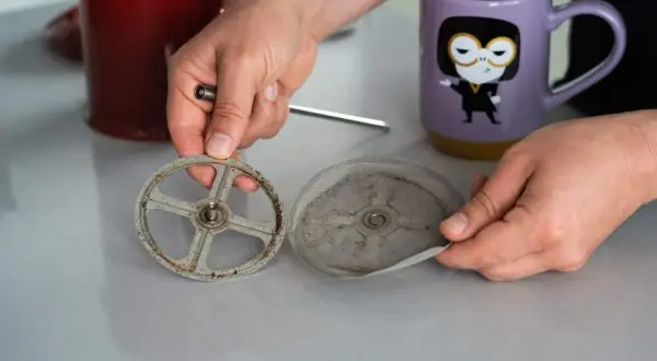 Hände zerlegen eine schmutzige French Press, um sie zu reinigen. Der Siebträger und das Sieb sind mit Kaffeesatz bedeckt.
