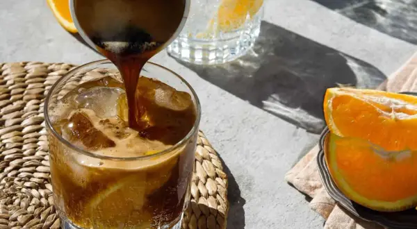 Espresso wird in ein Glas mit Eis und Orangenscheiben gegossen. Ein erfrischender Espresso Tonic für heiße Tage.
