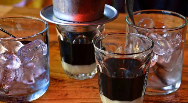 Zwei Gläser mit süßer Kondensmilch und starkem Kaffee, bereit für Eiswürfel. Ein vietnamesischer Eiskaffee zum Genießen.