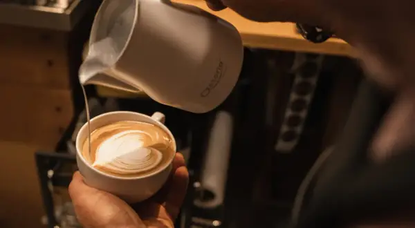 Barista kreiert ein Herz-Latte-Art-Muster, indem er Milchschaum in Kaffee gießt.
