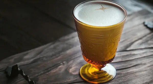 Ein goldener Becher mit cremigem Schaum, der an einen russischen Kaffee erinnert, steht auf einem rustikalen Holztisch.