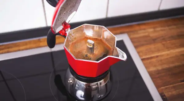 Roter Espressokocher auf dem Herd, der frischen Kaffee zubereitet. Der Duft von heißem Kaffee liegt in der Luft.