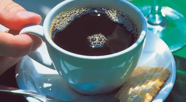 Eine Tasse schwarzer Kaffee mit Schaum, ein Keks und eine Löffel. So einfach ist, wie man schwarzen Kaffee macht.