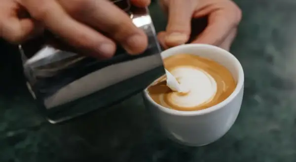 Barista gießt Milch in Kaffee, um ein Latte Art Herz zu kreieren.