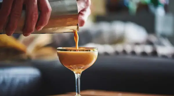 Ein cremiger Kaffee mit Alkohol wird aus einem Shaker in ein Glas gegossen. Ein köstlicher Kaffee-Cocktail, der zum Genießen einlädt.