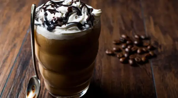 Eisgekühlter Kaffee mit Sahne und Schokoladensauce, ein köstliches Frappuccino Rezept. Daneben liegen geröstete Kaffeebohnen.