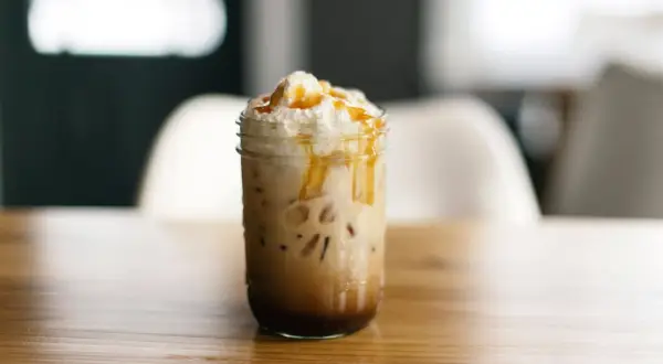 Ein köstlicher Caramel Frappuccino mit Sahne und Karamellsauce, serviert in einem Glas auf einem Holztisch.