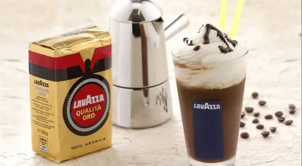 Ein köstlicher iced mocha mit Sahne und Schokoladensauce, daneben eine Packung Lavazza Qualità Oro Kaffee und eine Mokkakanne.