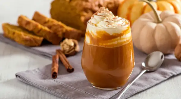 Ein cremiger Pumpkin Spice Latte mit Sahne und Zimt, daneben Kürbisbrot und Zimtstangen. Ein Genuss, der die pumpkin spice latte kalorien vergessen lässt.
